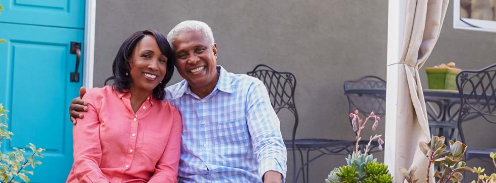 Image of a male and a female sitting in front of a house smiling